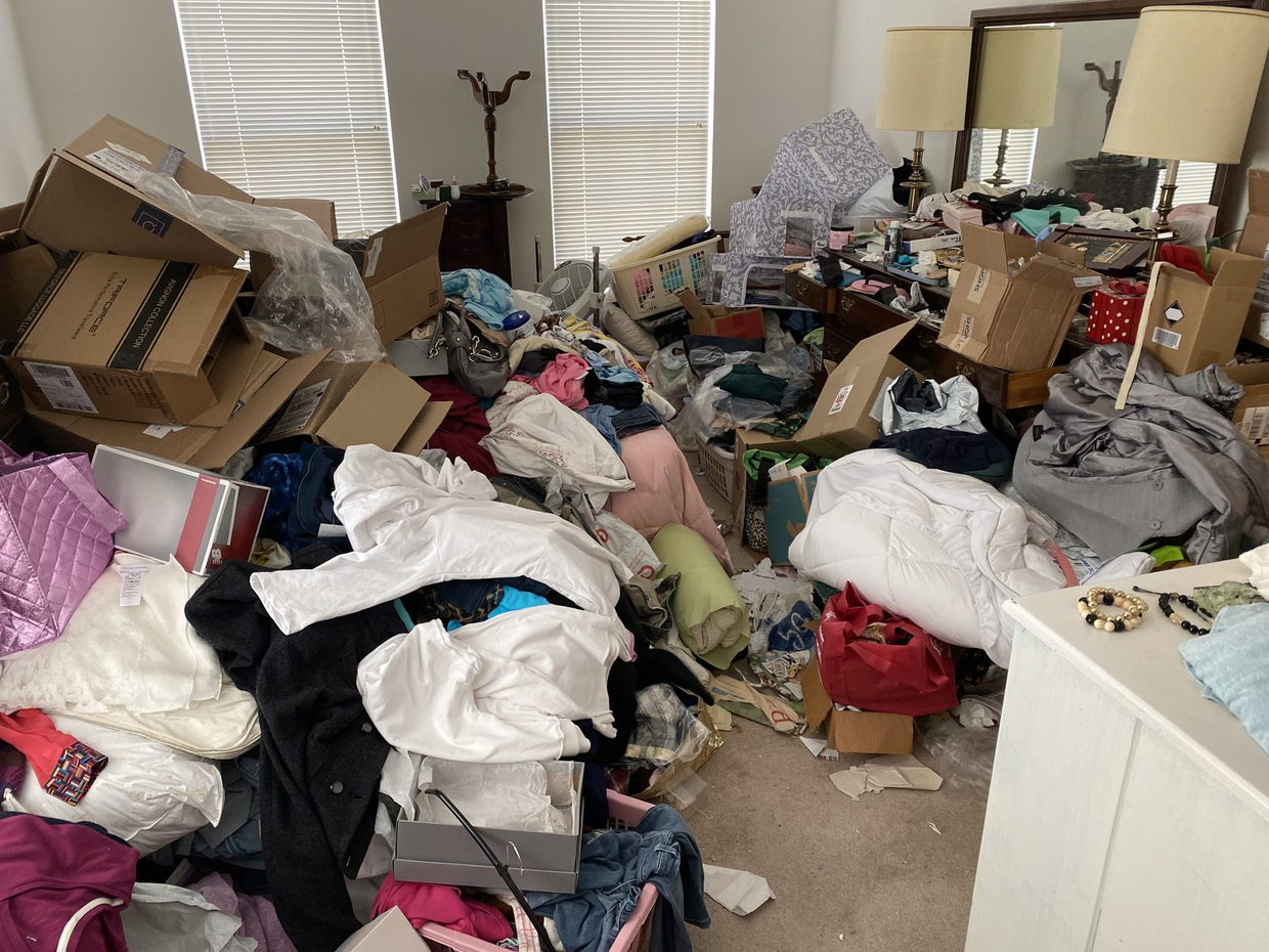 Bedroom with the floor completely covered in clothing, boxes and bedding