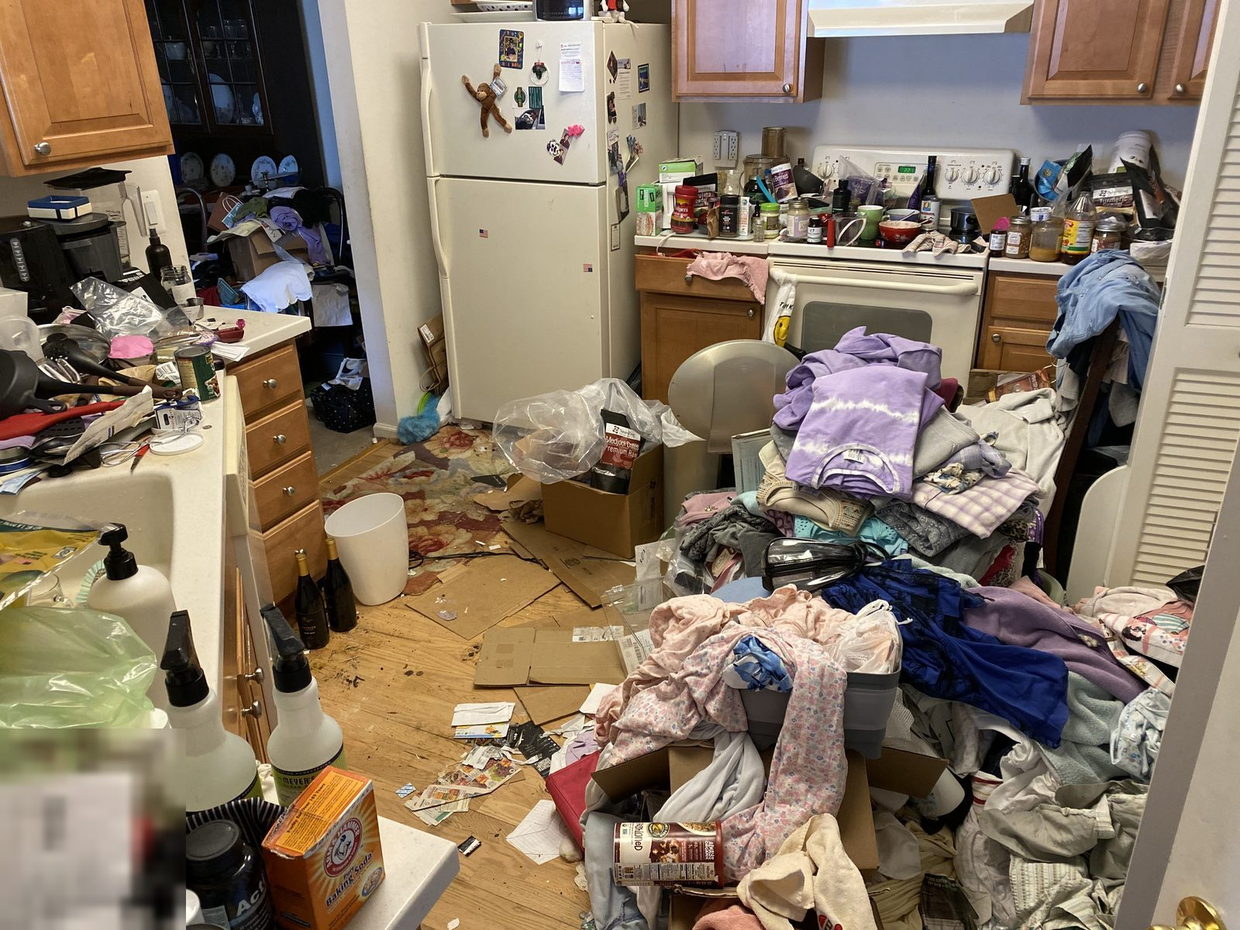 Kitchen with every counter covered and the floor stacked with clothing and cardboard